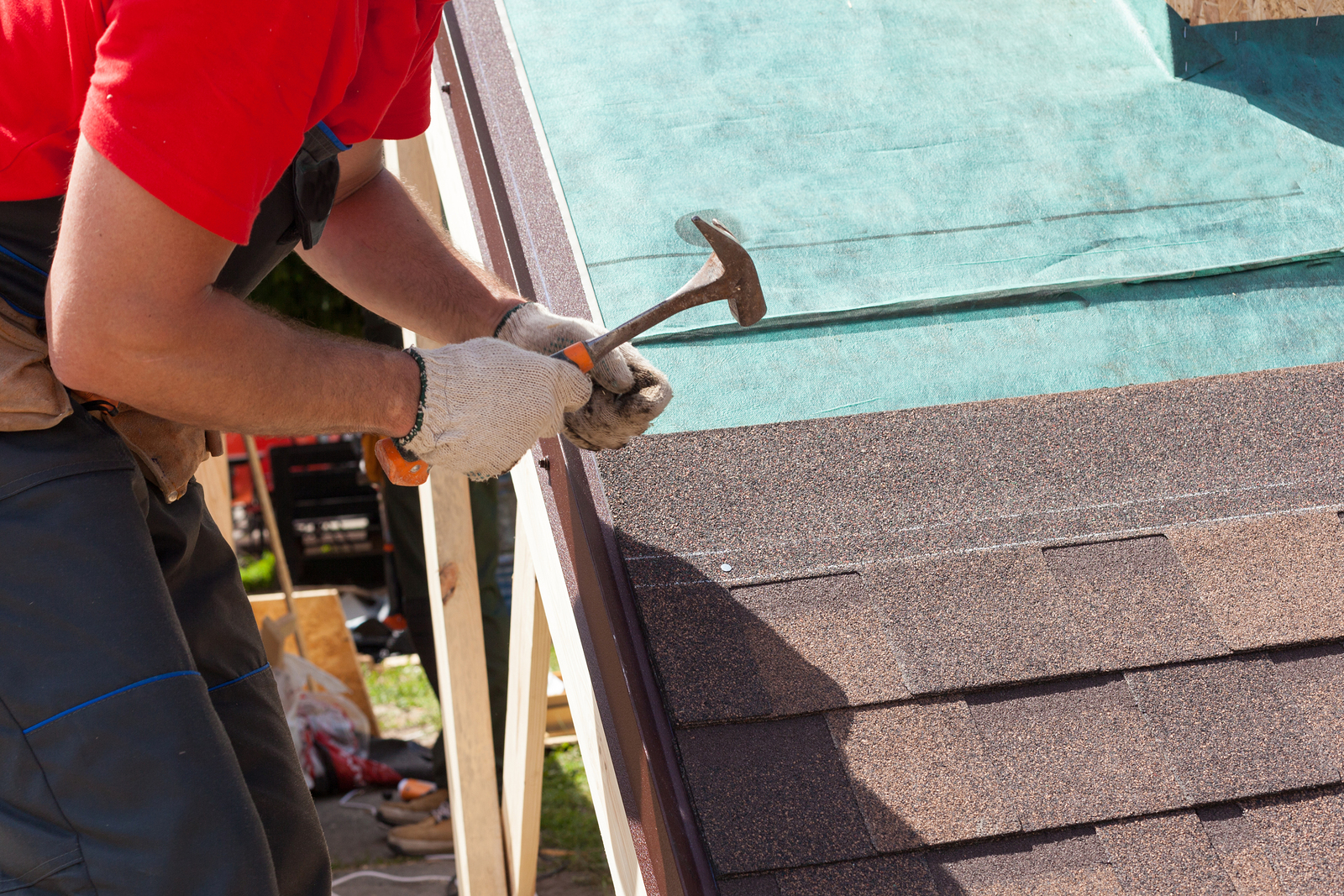Roofer builder worker use a hammer for installing roofing shingles